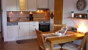 Cozinha compacta com eletrodomésticos modernos, mesa de jantar com cadeiras e um relógio de parede.
