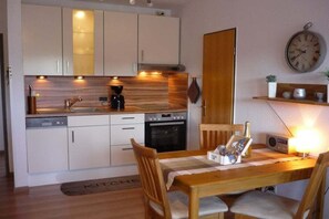 A compact kitchen with modern appliances, a dining table with chairs, and a wall clock. - Holiday apartment with 1 bedroom (Dornumersiel)