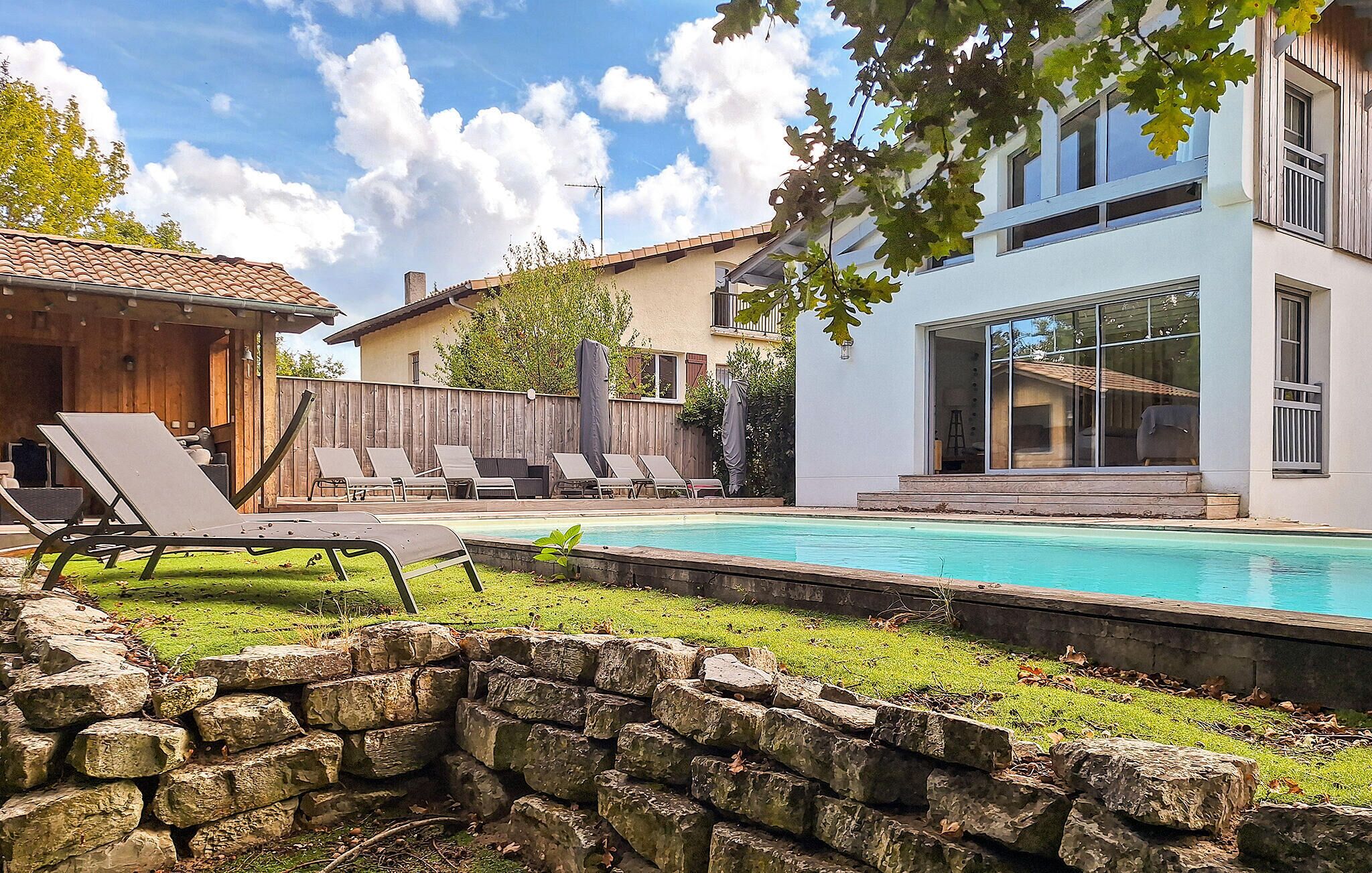 Uma casa moderna com piscina, espreguiçadeiras e uma parede de pedra.