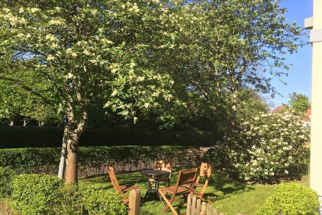 Une terrasse avec une table et des chaises, entourée d’une végétation luxuriante et d’arbres en fleurs.