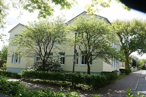 Ein zweistöckiges Gebäude mit heller Fassade, umgeben von Grünflächen und einem gepflasterten Weg.