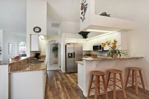 A modern kitchen with a central island, bar stools, stainless steel appliances, and a clock on the wall. - CCVS - Villa Tuscany with boat dock (Cape Coral SW FL)