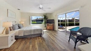 Quarto com cama, mesa de cabeceira, luminária, rack para TV e vista para uma piscina.