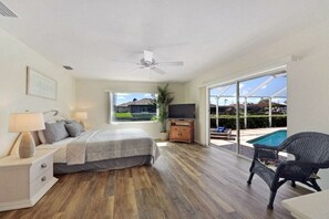 Ein Schlafzimmer mit Bett, Nachttisch, Lampe, TV-Schrank und Blick auf einen Swimmingpool.