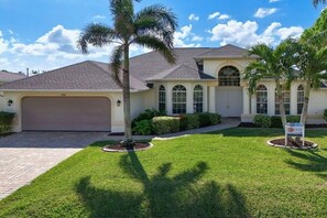 A residential house with a garage, a well-maintained lawn, and a palm tree. - CCVS - Villa Tuscany with boat dock (Cape Coral SW FL)