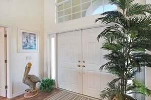 A hallway with a closed door, a potted plant, a pelican sculpture, and a framed picture on the wall. - CCVS - Villa Tuscany with boat dock (Cape Coral SW FL)