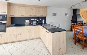 A kitchen with wooden cabinets, a built-in oven, a coffee maker, and a dining area with chairs and a table. - Nice home in Cancale with WiFi (Cancale)