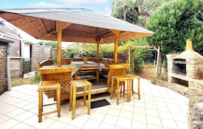 An outdoor patio with wooden furniture, a covered seating area, and a stone oven. - Nice home in Cancale with WiFi (Cancale)