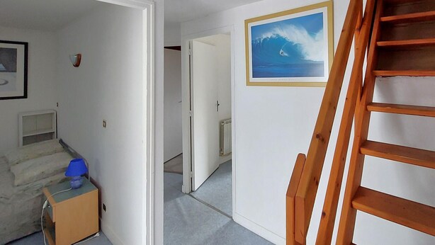 En hall med en trätrappa, en inramad tavla som föreställer en våg och ett element.