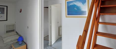 Un couloir avec un escalier en bois, un tableau encadré représentant une vague et un radiateur.