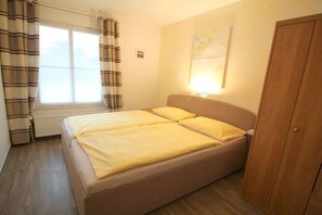 A single bed with a headboard, a window with curtains, a radiator, and a wooden wardrobe. - holiday home at the harbor (Zingst)
