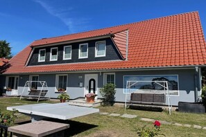A two-story house with a red-tiled roof, a front porch with a swing set, and a small garden area. - holiday home at the harbor (Zingst)