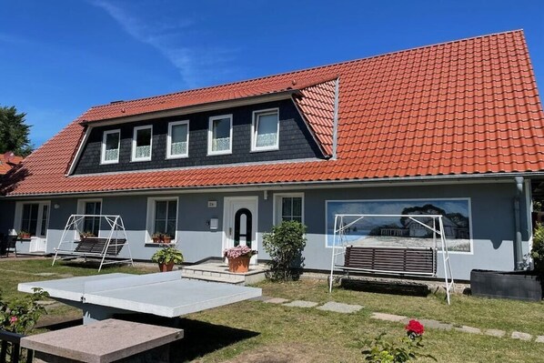 A two-story house with a red-tiled roof, a front porch with a swing set, and a small garden area. - holiday home at the harbor (Zingst)
