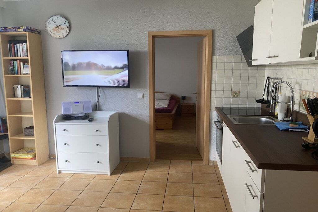 Une cuisine de taille réduite, équipée d’une télévision, d’une bibliothèque et d’une porte donnant accès à une chambre.