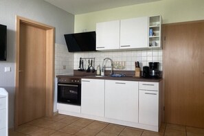 A compact kitchen with white cabinets, a black oven, a coffee maker, and a TV mounted above the counter. - holiday home at the harbor (Zingst)