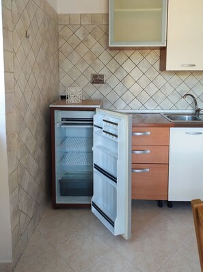 Eine kleine Küche mit integriertem Kühlschrank, einer Spüle und einem Schrank über der Arbeitsplatte.