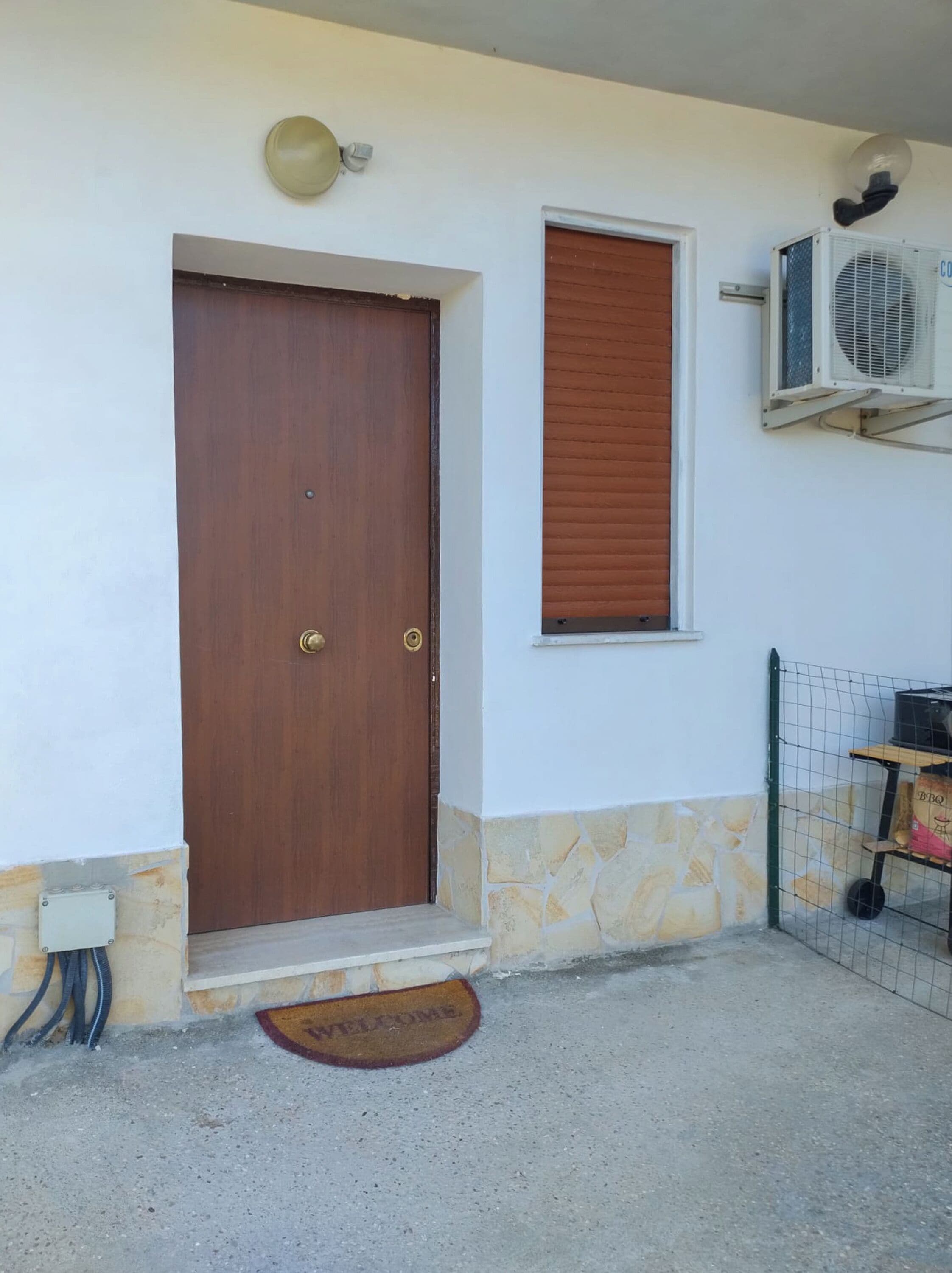 A wooden door with a brass handle, a small window with a shutter, and a wall-mounted air conditioning unit.