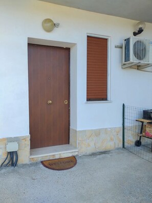 Eine Holztür mit Messingklinke, ein kleines Fenster mit Rollo und eine Wand-Klimaanlage.