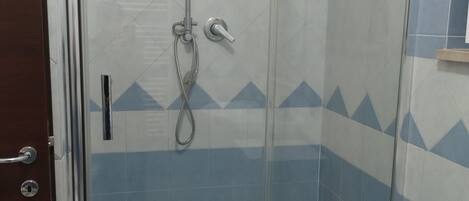 Une cabine de douche fermée par des parois en verre, équipée d’un pommeau de douche à main et d’un robinet à main.