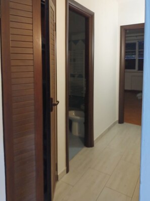 Passadís amb una porta de fusta, una porta de vidre que dona a un bany i una finestra amb persianes.