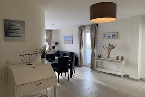 Ein modernes Wohnzimmer mit Essbereich, einem weißen Konsolentisch, einem schwarzen Sofa und einem großen Fenster mit Vorhängen.