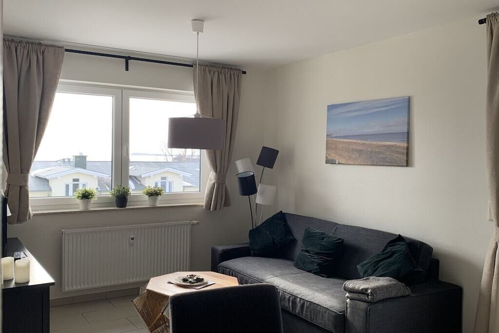 Un salon moderne avec un canapé, une table sur laquelle se trouve une lampe, et une vue sur les immeubles par la fenêtre.