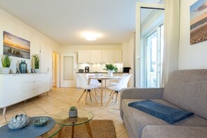 A modern living room with a sofa, a glass coffee table, and a dining area with a white table and chairs. - Anchorage - Binz Stars (Ostseebad Binz)