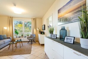 A living room with a sofa, armchair, coffee table, and a view of the outdoors through a window. - Anchorage - Binz Stars (Ostseebad Binz)