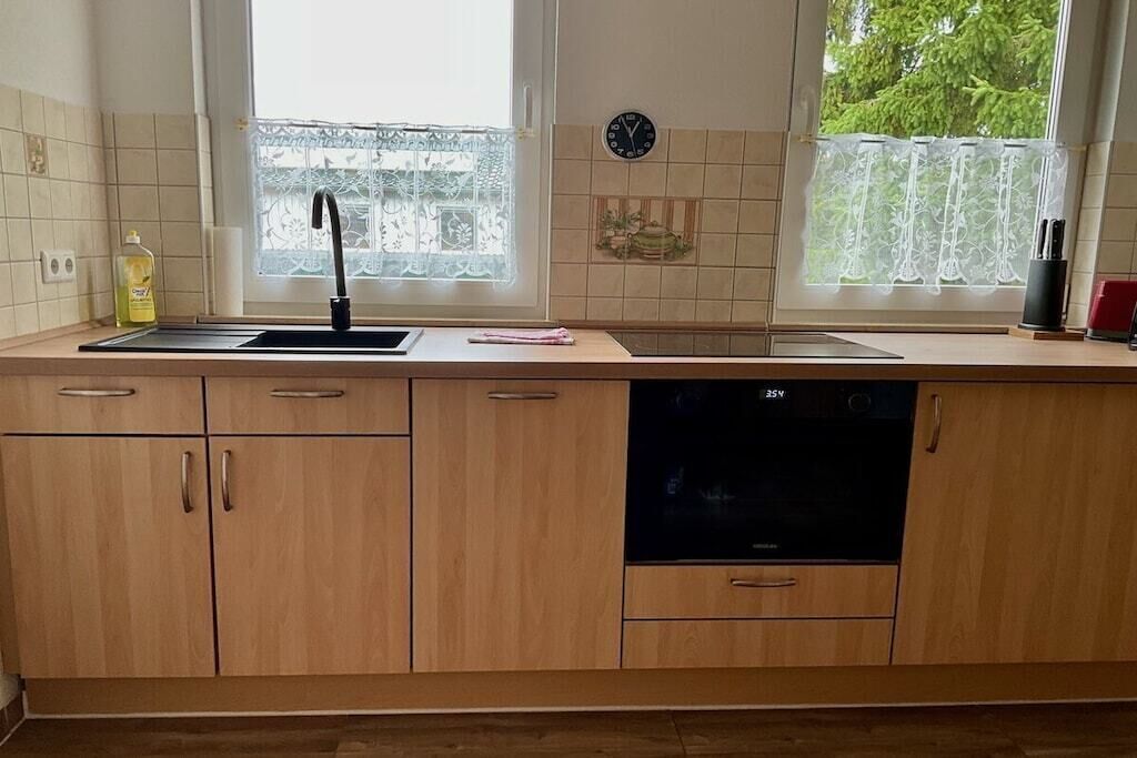 A kitchen with wooden cabinets, a black dishwasher, and a window with lace curtains.