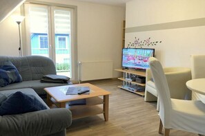 A living room with a sofa, a coffee table, a TV, and a chair. - Holiday apartment type 04-S in the attic (Zingst)