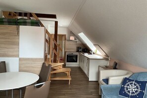 A compact living space with a dining area, kitchenette, and a loft bedroom with a view. - Holiday apartment type 04-S in the attic (Zingst)