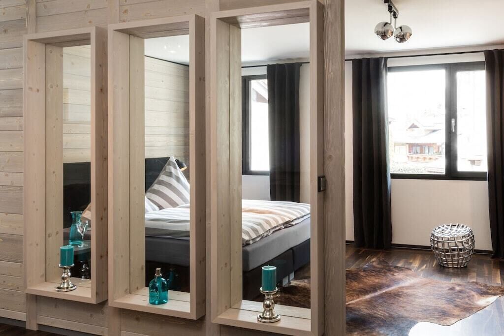 A bedroom with a bed, a window with curtains, and a mirror with a candle on a shelf.
