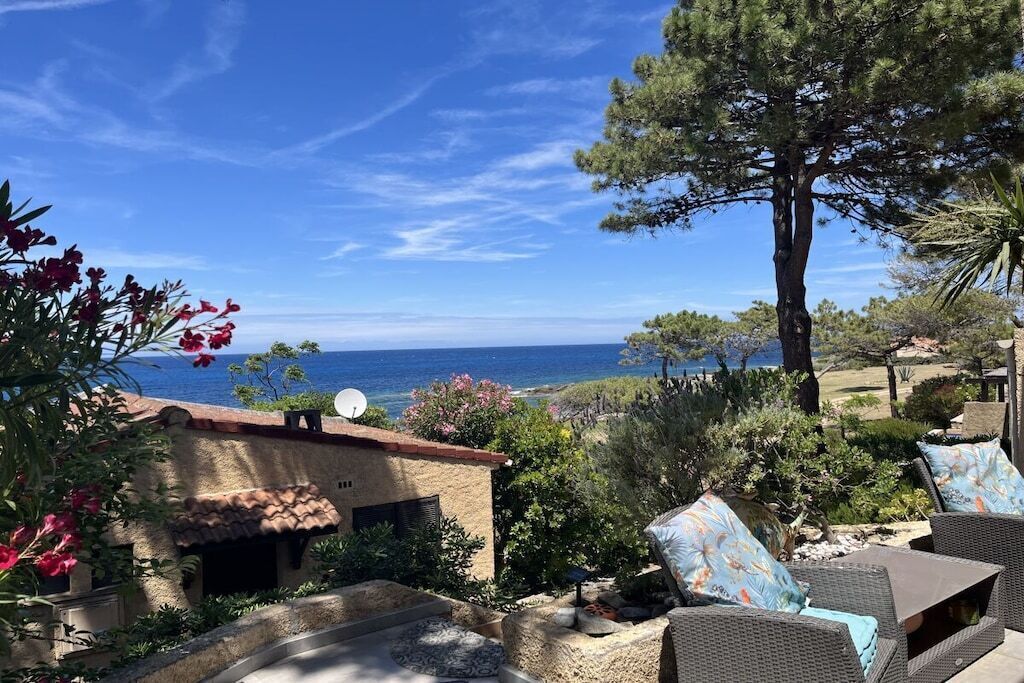 A patio area with outdoor furniture, a view of the sea, and a large tree.