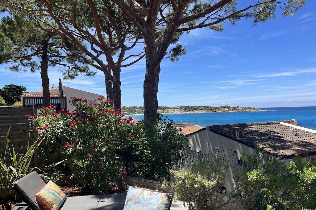A patio with a view of the sea, a wooden fence, and a chair with a cushion.