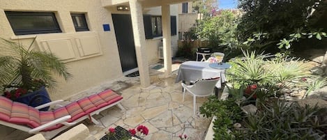 Un patio con suelo de piedra, una silla de descanso, una mesa con sillas y diferentes macetas con plantas.