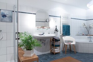 Een moderne badkamer met een glazen douchecabine, een wit wastafelmeubel met spiegel, een badkuip en een houten bankje.