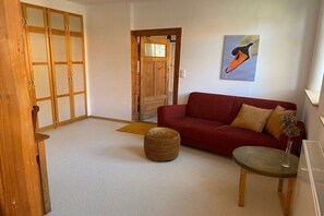 A living room with a red sofa, a round ottoman, a small table with a vase, and a wooden door. - Holiday apartment with 5 bedrooms (Strachau)