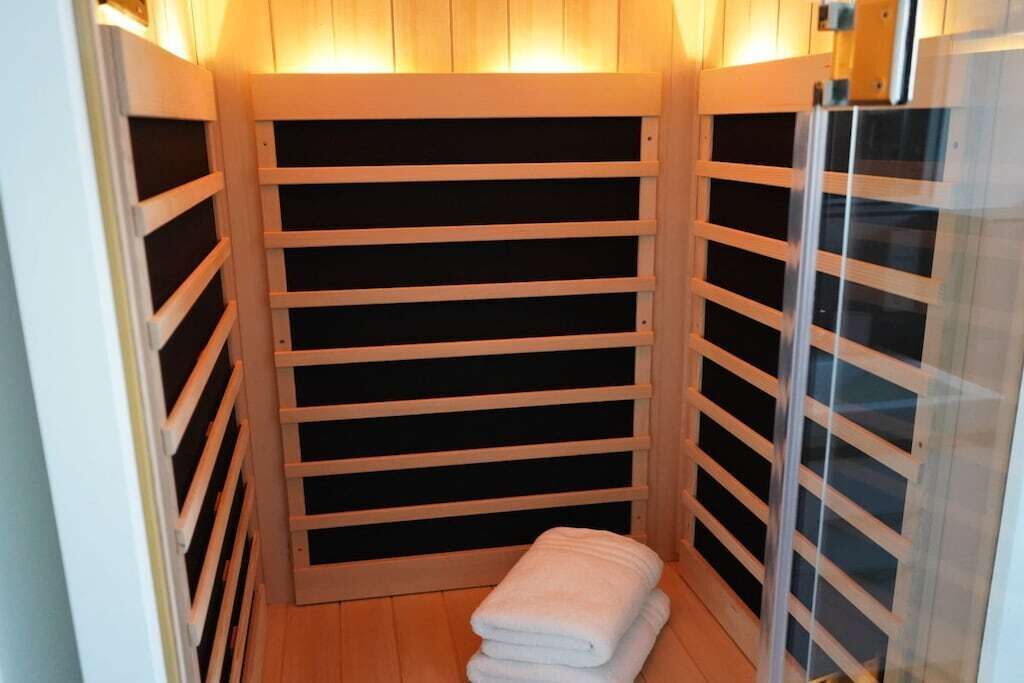 A small, enclosed space with a wooden slatted partition, a glass door, and a stack of white towels on the floor.