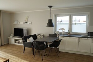 A modern kitchen with a dining area, white cabinetry, a black pendant light, and a view of a body of water through the window. - Holiday apartment in Boizenburg with sauna (Boizenburg)