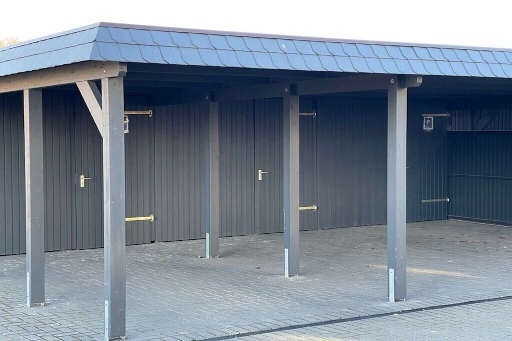 Un espace extérieur abrité, doté de piliers en métal et d’un toit, probablement utilisé comme zone de stationnement ou de chargement.