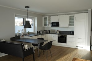 A modern kitchen with white cabinets, a black microwave, and a dining area with a table and chairs. - Holiday apartment in Boizenburg with sauna (Boizenburg)