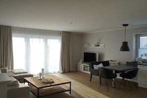 A modern living room with a sofa, a coffee table, a TV, and a dining area with chairs and a table. - Holiday apartment in Boizenburg with sauna (Boizenburg)