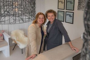 Two individuals standing at a reception desk with a white chair and a decorative wall piece in the background. - Holiday home in Renesse with swimming pool (Renesse)