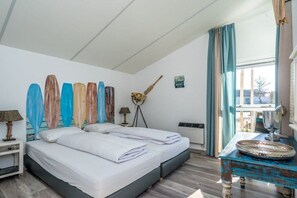 A bedroom with two beds, a window with curtains, a wall-mounted lamp, and a decorative wall piece. - Holiday home in Renesse with swimming pool (Renesse)