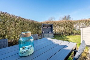 An outdoor seating area with a table and chairs, a glass jar with a blue liquid, and a covered seating area in the background. - Holiday home in Renesse with swimming pool (Renesse)