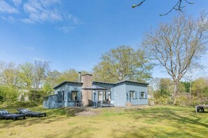 Ein zweistöckiges Haus mit einer Terrasse, einem Schornstein und einem Rasen.