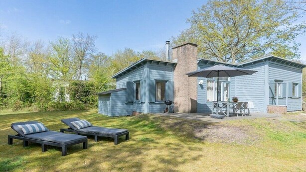 A two-story house with a chimney, a barbecue grill, and a patio with lounge chairs. - Holiday home with 2 bedrooms (Burgh-Haamstede)
