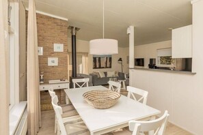 Ein modernes Interieur mit einem Essbereich, der einen weißen Tisch und Stühle, eine gewebte Tischdekoration und eine Hängelampe zeigt.