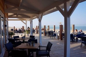 Ein Essbereich im Freien mit Holztischen und -stühlen mit Blick auf einen Strand.