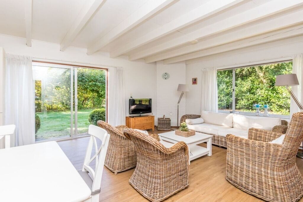 A furnished living room with a television, wicker furniture, and a view of the garden.